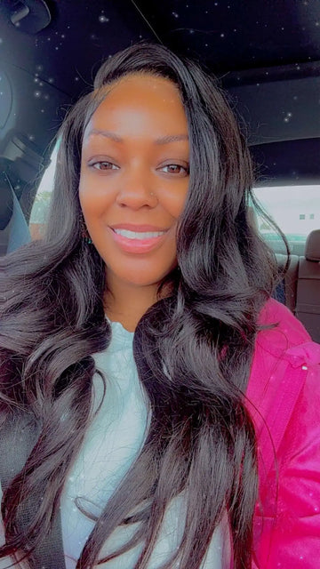 A woman with long, dark wavy hair wearing a bright pink jacket over a light blue top.
